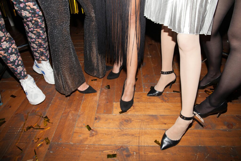 Women's legs in stylish outfits and footwear at a lively indoor party.