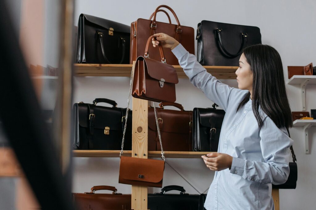 Asian woman browsing a variety of leather handbags in a showroom, showcasing elegance and style.